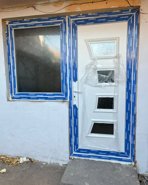 Derë e bardhë hyrëse me xham dekorativ dhe dritare në anën e majtë